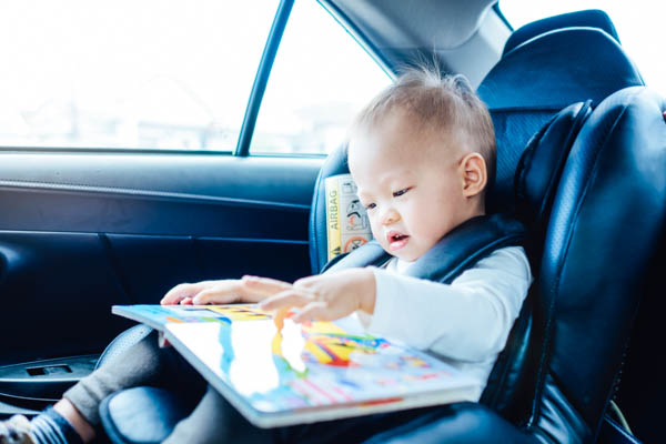Baby sitzt im Kindersitz im Auto und blättert durch ein Bilderbuch