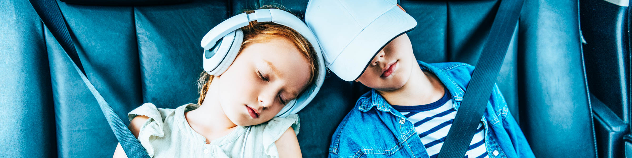 Zwei Kinder schlafen auf der Rückbank eines Autos, das Mädchen trägt Kopfhörer